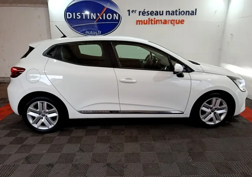 Profil droit d'une Renault Clio Business Blue dCi 85 blanche, avec jantes alliage et logo Distinxion en arrière-plan.