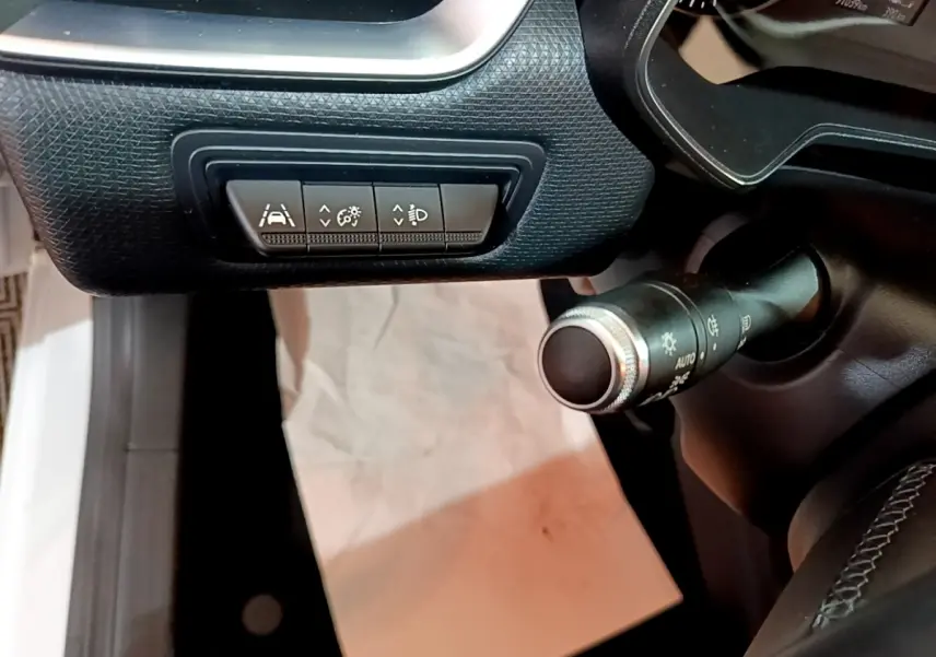 Gros plan sur les commandes d'assistance et éclairage côté gauche du tableau de bord noir d'une Renault Clio blanche 2020.