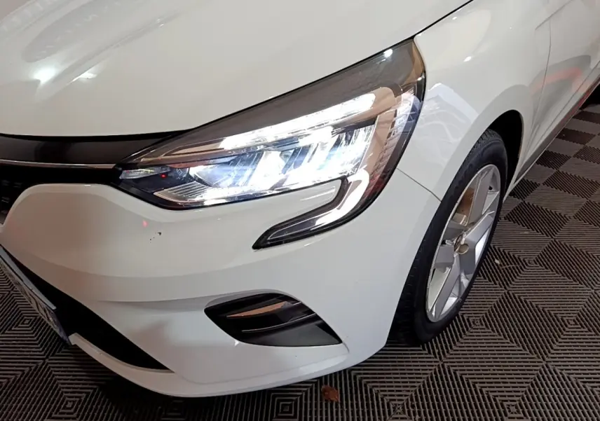 Gros plan sur l'avant droit blanc d'une Renault Clio 2020 avec phare LED allumé et jante alliage visible.