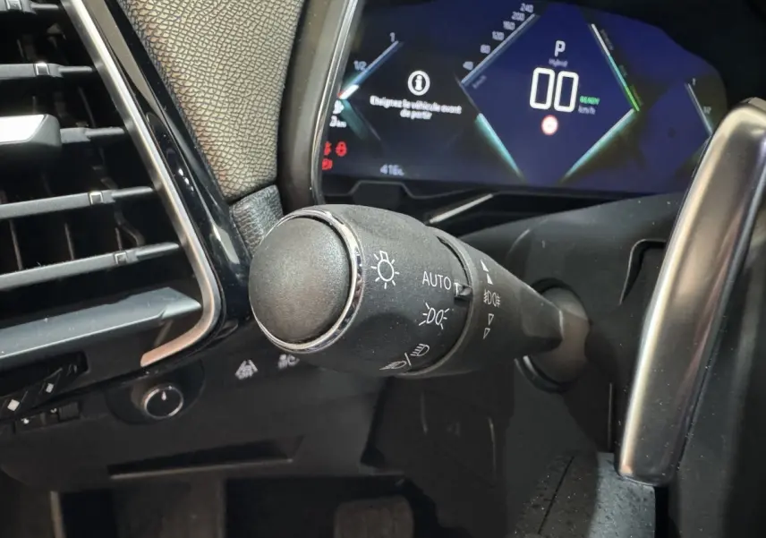 Gros plan sur la commande des phares et le tableau de bord numérique du DS7 Crossback E-TENSE gris foncé.