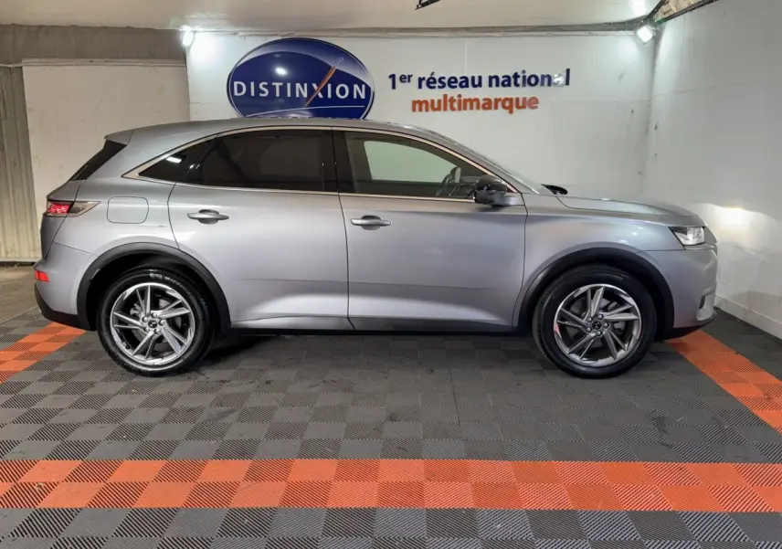 Vue de profil côté gauche d'un DS7 Crossback E-TENSE gris foncé dans un showroom avec sol à damier noir et orange.