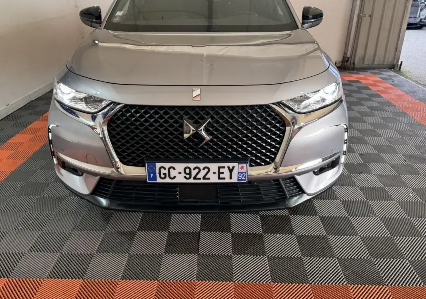 Vue avant d'un DS7 Crossback gris foncé avec calandre noire à motif losange et phares LED allumés.