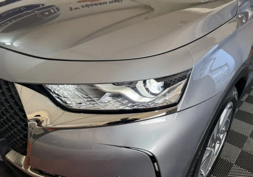 Gros plan sur le phare avant droit du DS7 Crossback E-TENSE gris foncé, mettant en valeur la calandre et la jante alu.