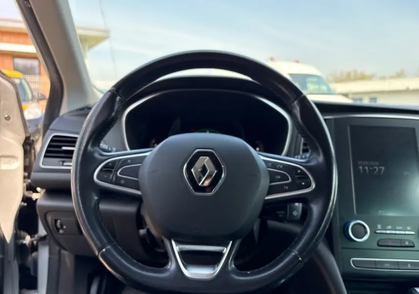 Vue intérieure centrée sur le volant cuir noir de la Renault Mégane Intens, avec écran tactile et tableau de bord visibles.