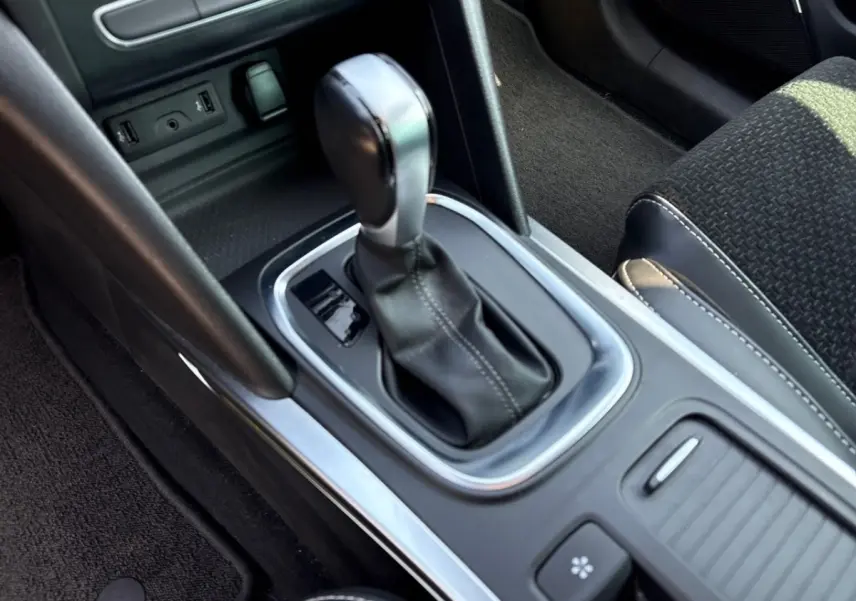 Gros plan sur la console centrale noire de la Renault Mégane avec levier de vitesse automatique et sellerie tissu noire.