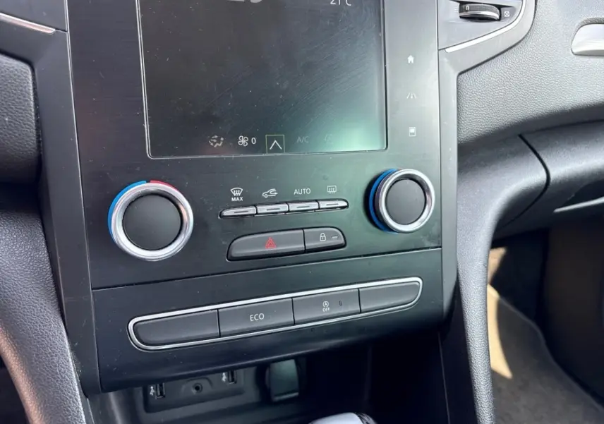 Vue rapprochée du tableau de bord central noir de la Renault Mégane Intens avec commandes climatisation et écran tactile.