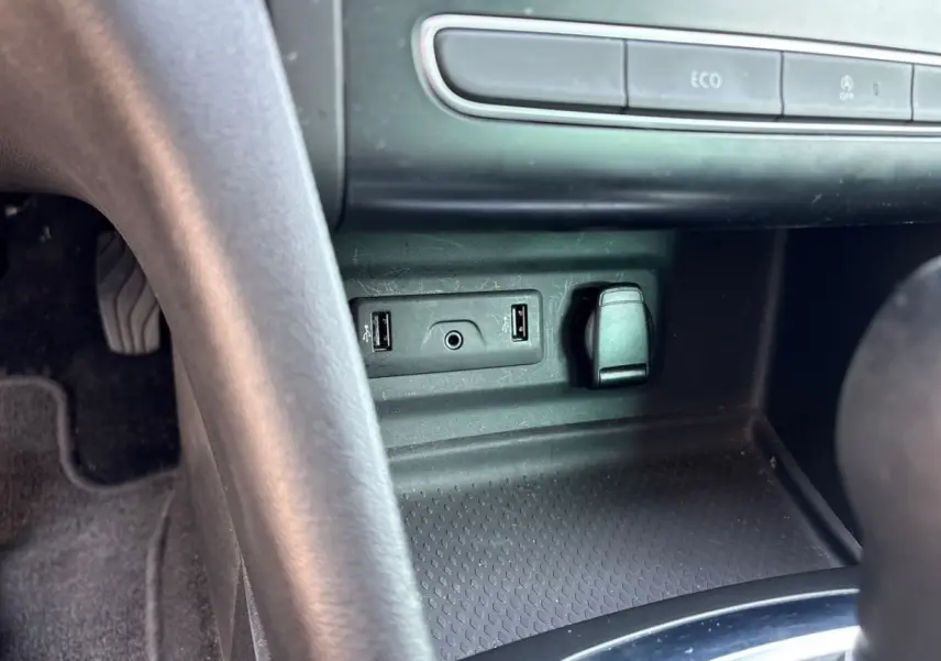 Vue rapprochée de la console centrale noire de la Renault Mégane Intens, montrant ports USB et prise 12V.