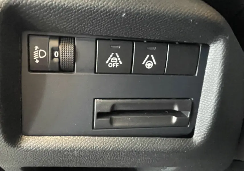 Gros plan sur les commandes noires du tableau de bord du Citroën C5 Aircross hybride 2025, avec réglage des phares et aides à la conduite.