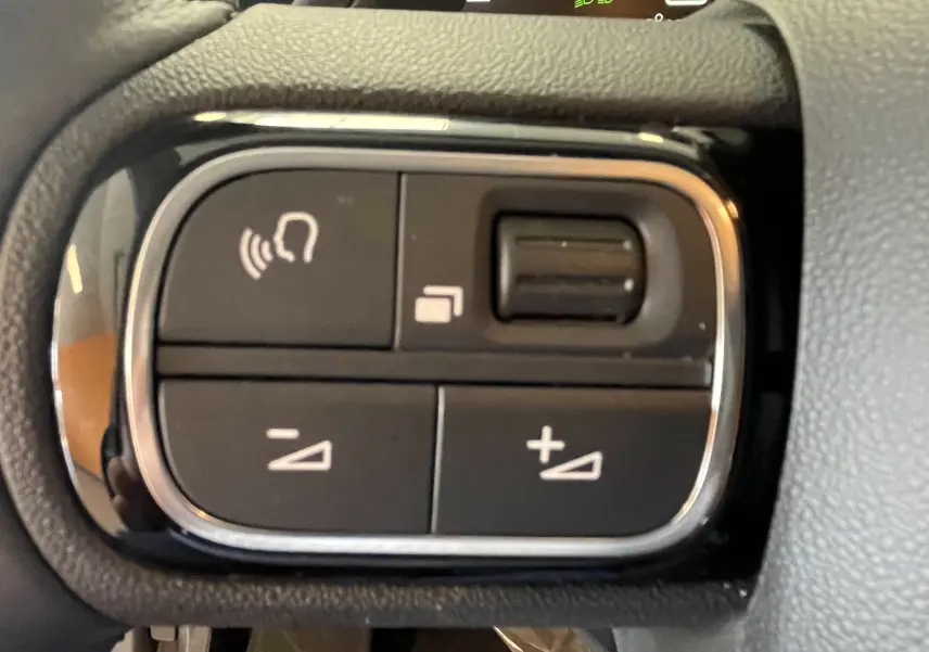 Gros plan sur les commandes de volume au volant du Citroën C5 Aircross hybride 2025, finition noire avec contour chromé.
