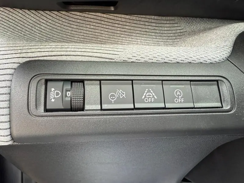 Vue rapprochée des commandes noires de réglage des phares et aides à la conduite sur fond tissu gris clair dans une Citroën C3 gris Mercury.