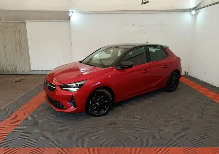 Opel Corsa rouge 2023 vue 3/4 avant droit, toit noir, jantes alliage noires, dans un garage éclairé.