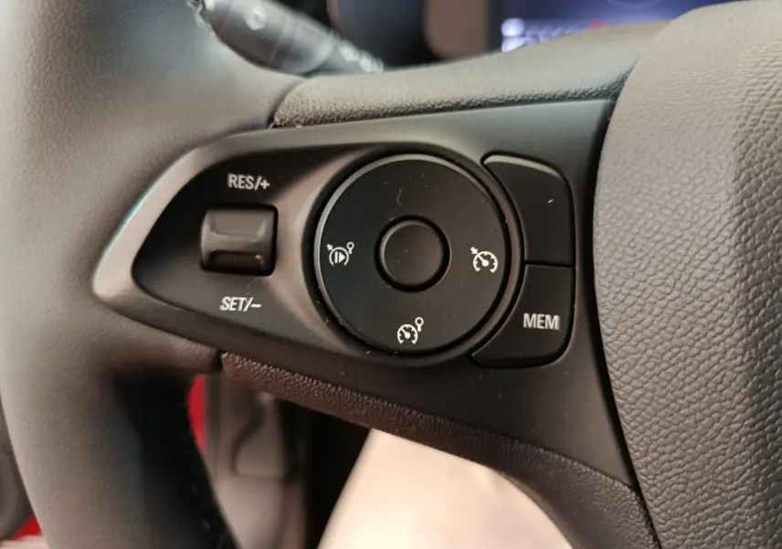 Gros plan sur les commandes de régulateur de vitesse au volant cuir noir de l’Opel Corsa rouge 2023.