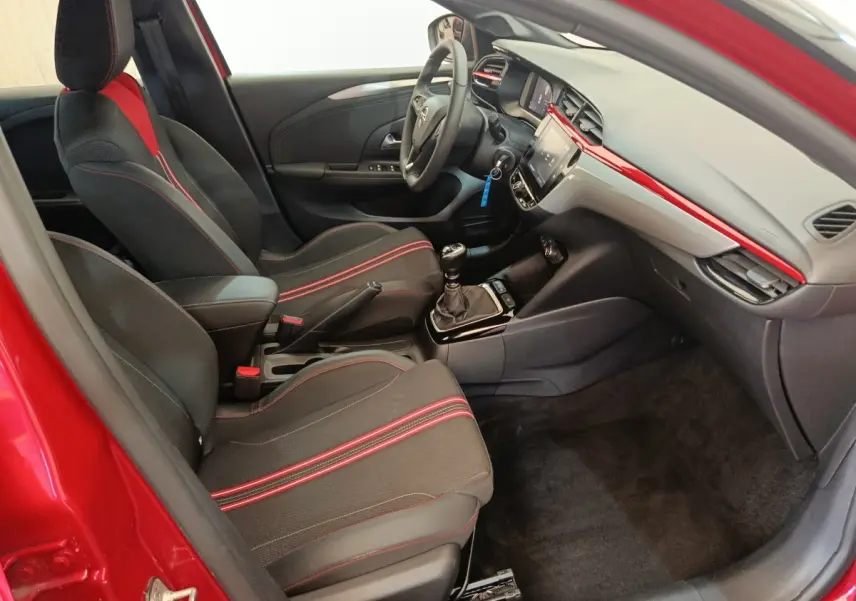 Intérieur avant droit de l’Opel Corsa rouge 2023, sièges noirs avec surpiqûres rouges et tableau de bord moderne.