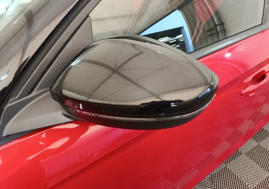 Gros plan sur le rétroviseur noir côté gauche de l’Opel Corsa rouge 2023, avec porte visible en arrière-plan.