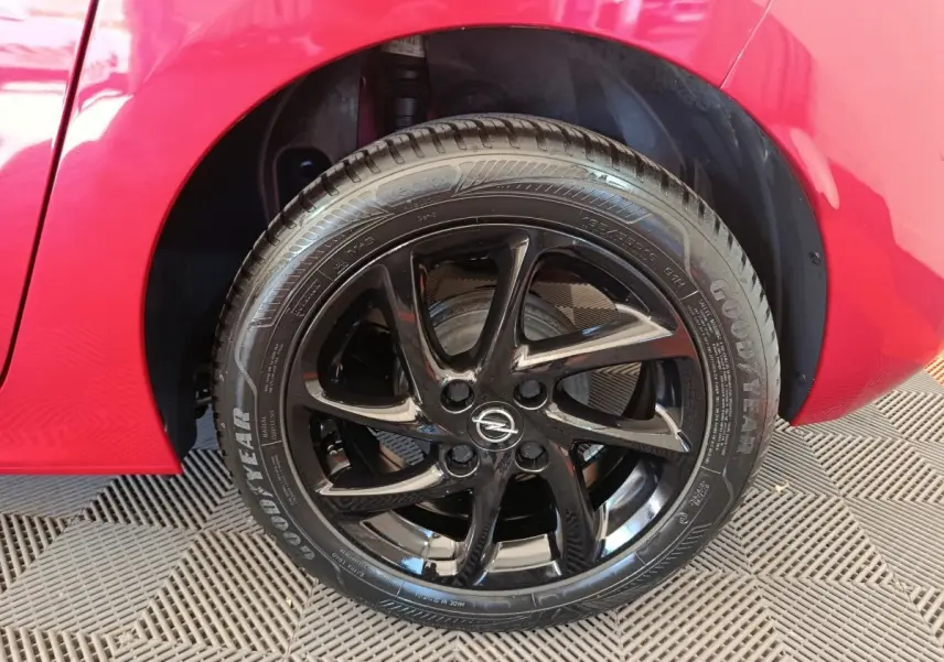 Gros plan sur la roue avant droite noire brillante d’une Opel Corsa rouge 2023, avec logo Opel au centre.