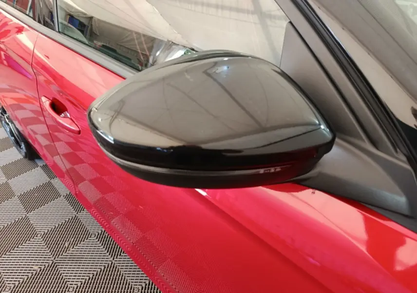 Gros plan sur le rétroviseur noir côté gauche d’une Opel Corsa rouge 2023, avec poignée de porte visible.