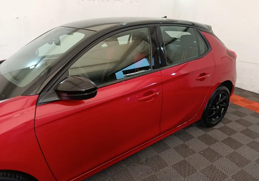 Vue latérale droite d'une Opel Corsa rouge 2023 avec toit noir et jantes noires brillantes.