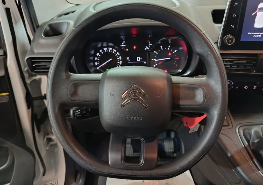 Vue rapprochée du volant noir de la Citroën Berlingo blanc, avec tableau de bord et écran tactile visibles.