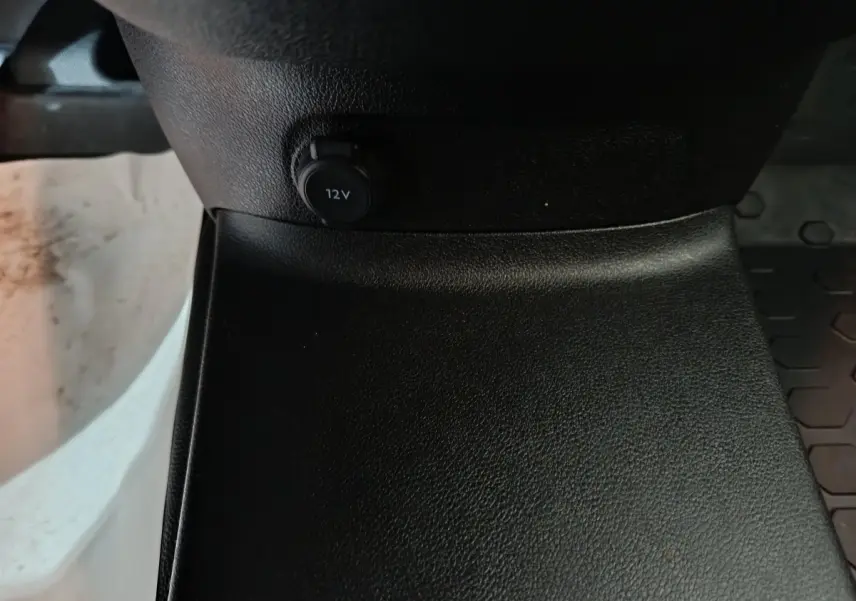 Prise 12V noire en gros plan sur la console centrale du Citroën Berlingo blanc, vue intérieure basse.