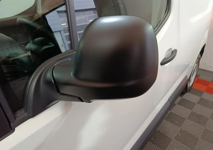 Gros plan sur le rétroviseur noir côté gauche du Citroën Berlingo blanc, avec partie de la porte visible.