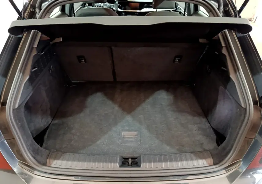 Coffre ouvert vu de l'arrière d'une Audi A3 gris foncé, montrant l'espace de chargement vide et la tablette de coffre.