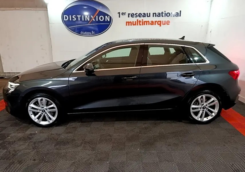 Audi A3 gris foncé vue de profil côté gauche, avec jantes alliage et toit ouvrant en intérieur showroom.