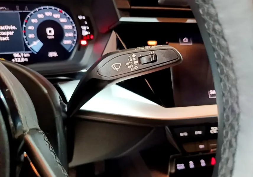 Gros plan sur la manette d’essuie-glace et le tableau de bord numérique bleu d’une Audi A3 gris foncé, vue côté conducteur.