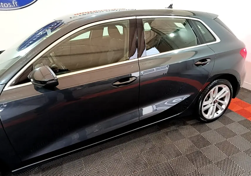 Vue de profil côté gauche d'une Audi A3 gris foncé avec jantes alliage et rétroviseurs noirs brillants.