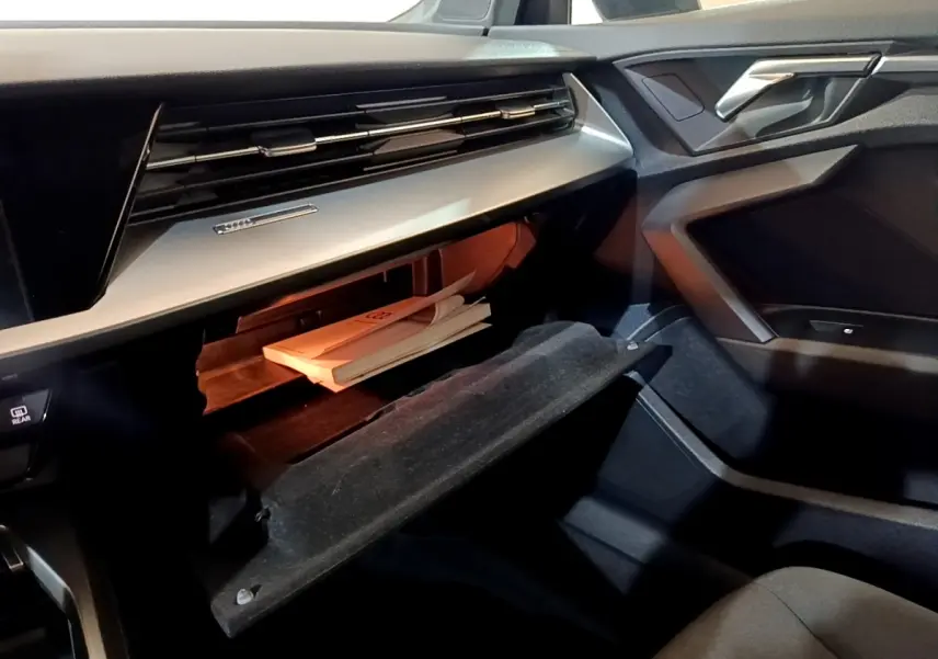 Intérieur côté passager de l'Audi A3 gris foncé 2021, boîte à gants ouverte avec documents visibles.