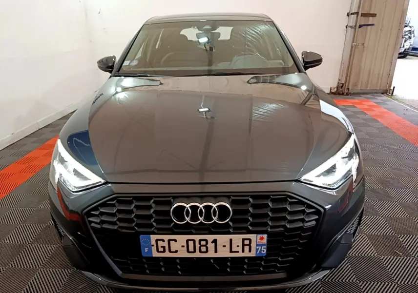 Vue avant d'une Audi A3 gris foncé avec calandre noire et phares LED allumés dans un garage.