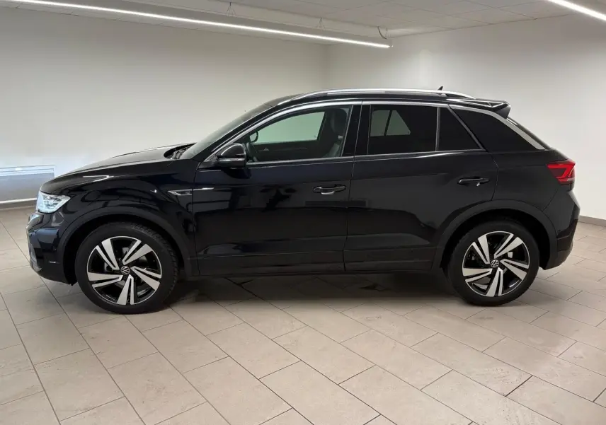 Vue de profil côté gauche du Volkswagen T-Roc 1.5 TSI 150 DSG7 R-Line Edition noir intense dans un intérieur neutre.
