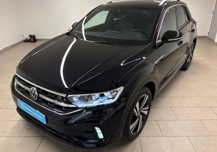 Volkswagen T-Roc noir intense en 3/4 avant droit, avec phares LED allumés et jantes R-Line distinctives.