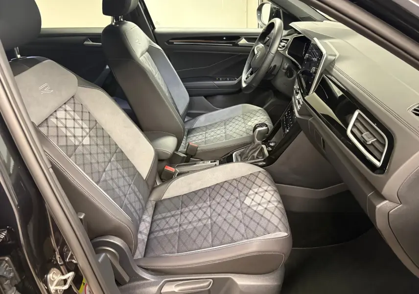 Vue intérieure côté conducteur du Volkswagen T-Roc 1.5 TSI R-Line 2025 avec sièges tissu et alcantara gris à motifs.