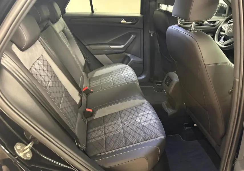 Vue intérieure côté gauche sur les sièges arrière en cuir noir et tissu à motif du Volkswagen T-Roc 2025 noir intense.