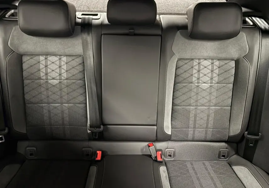 Vue intérieure arrière des sièges arrière du Volkswagen T-Roc 2025, tissu gris à motifs avec appuie-têtes et ceintures visibles.