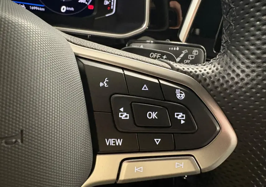 Gros plan sur les commandes du volant noir perforé du Volkswagen T-Roc 1.5 TSI 150 DSG7 R-Line Edition.