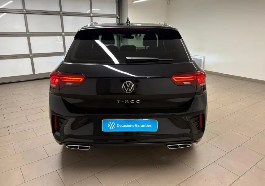 Vue arrière du Volkswagen T-Roc noir intense 2025 avec feux allumés et double sortie d'échappement chromée.