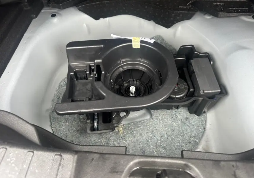 Gros plan sur le rangement de la roue de secours dans le coffre du Jeep Avenger 2025, structure plastique noire et fond gris clair.