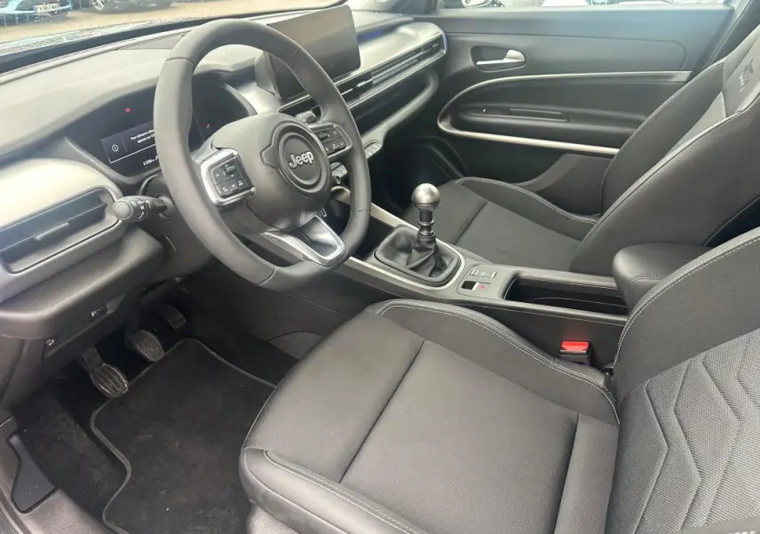 Vue intérieure côté conducteur du Jeep Avenger 2025, volant cuir, boîte manuelle, sièges noirs avec surpiqûres blanches.