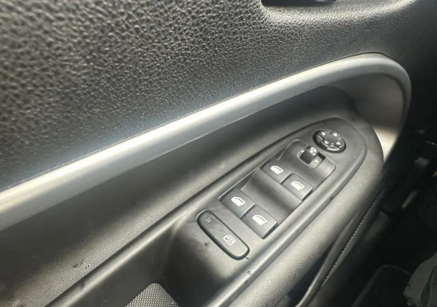 Gros plan sur les commandes électriques des vitres et des rétroviseurs côté conducteur du Jeep Avenger gris foncé 2025.