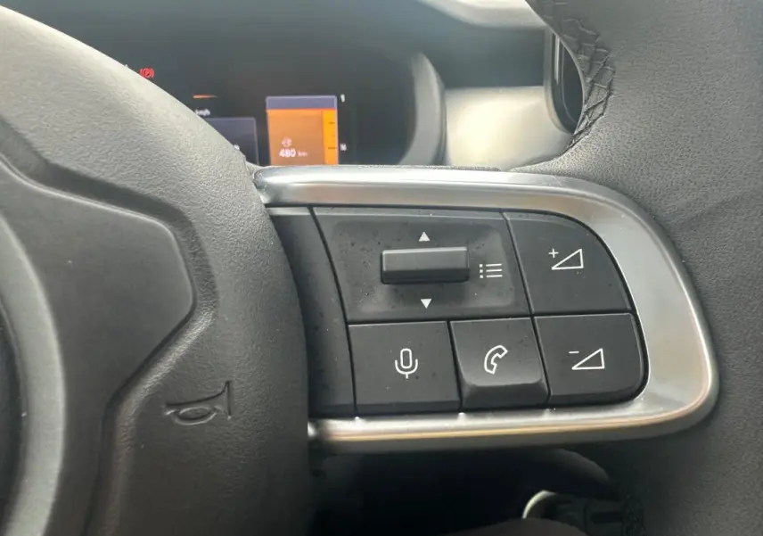 Gros plan sur les commandes du volant cuir du Jeep Avenger gris foncé, avec boutons de volume et téléphone visibles.