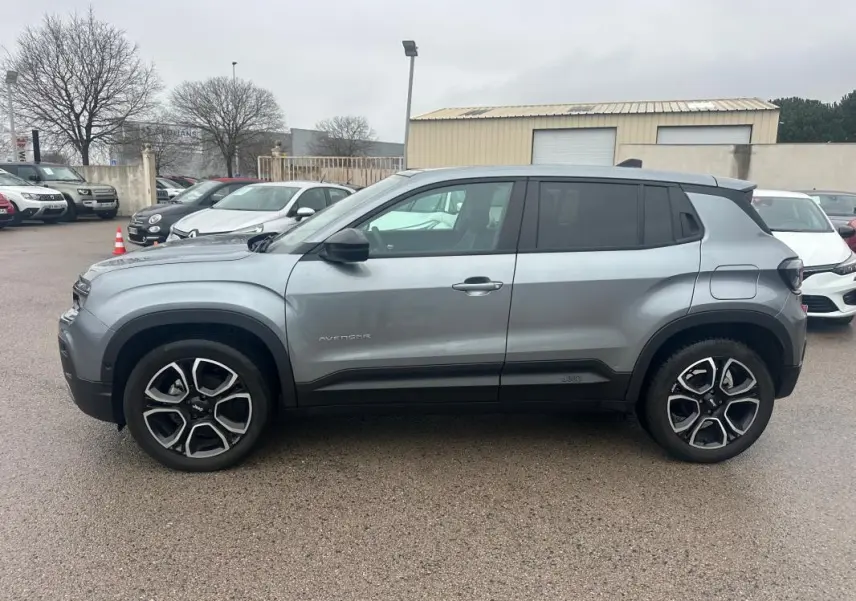 Vue de profil côté gauche d'un Jeep Avenger gris foncé avec jantes alliage 18 pouces sur parking extérieur.
