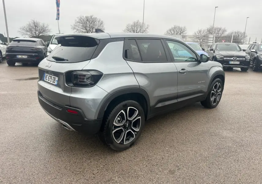 Vue 3/4 arrière droite d’un Jeep Avenger gris foncé avec jantes alliage 18 pouces et toit noir sur parking.