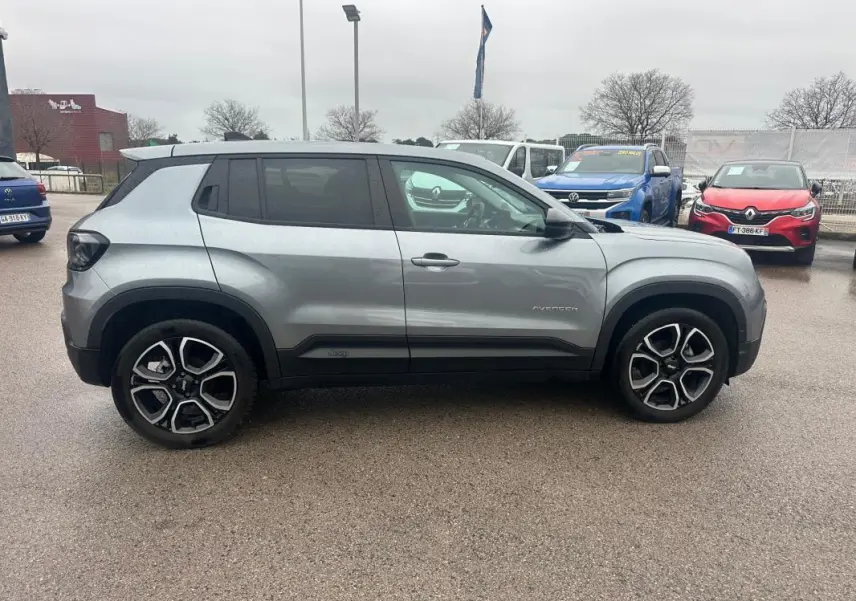 Vue de profil côté gauche d'un Jeep Avenger gris foncé avec jantes alliage 18 pouces sur parking extérieur.