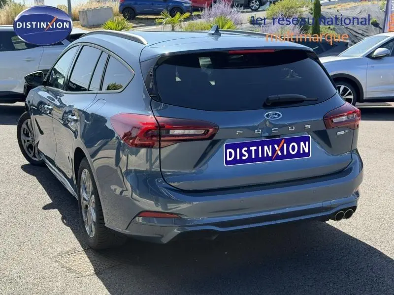 Vue 3/4 arrière droite d'une Ford Focus SW 2023 bleu azur métallisé avec double sortie d'échappement et toit ouvrant.