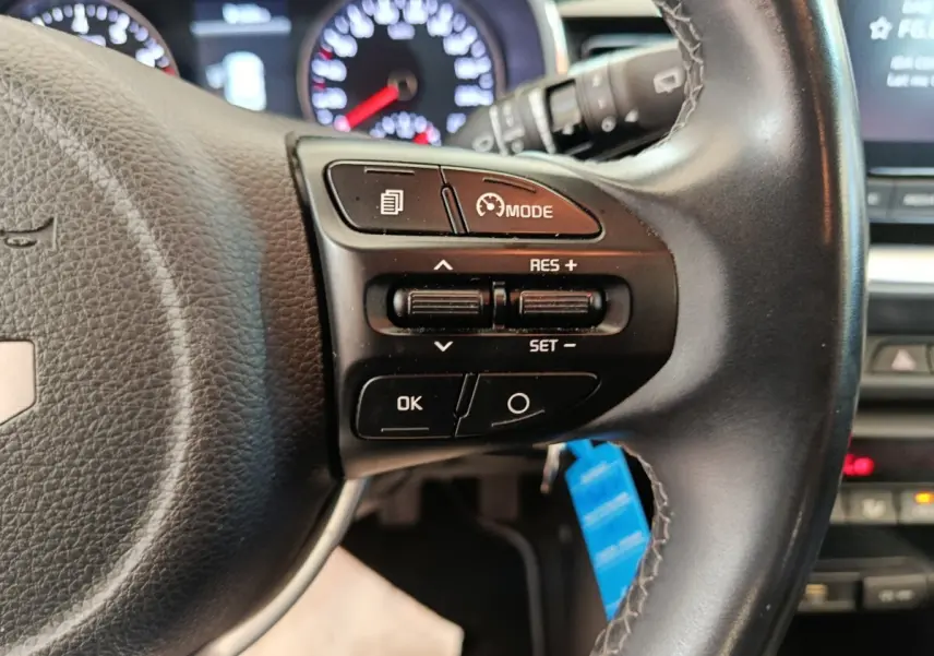 Gros plan sur le volant cuir noir du Kia Stonic 2023, avec commandes multifonctions et tableau de bord lumineux en arrière-plan.