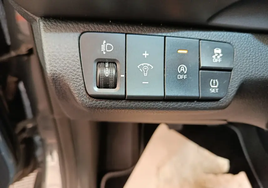 Gros plan sur les commandes de réglage des phares et aides à la conduite dans une Kia Stonic gris foncé, intérieur noir.