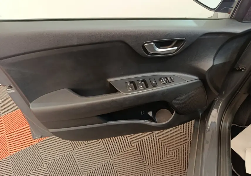 Vue rapprochée de la porte avant gauche grise du KIA STONIC 2023 avec commandes électriques et poignée intérieure chromée.