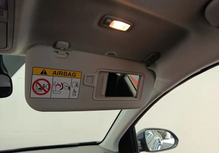 Vue intérieure côté conducteur du pare-soleil déplié avec miroir et avertissement airbag dans un Kia Stonic gris foncé 2023.