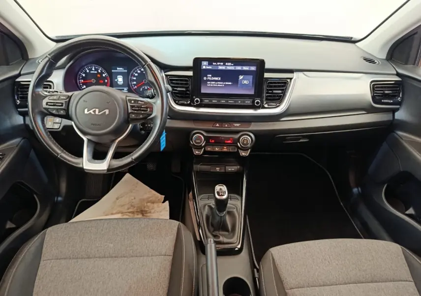 Vue intérieure frontale du tableau de bord gris et noir de la KIA Stonic 2023 avec volant cuir et écran tactile central.